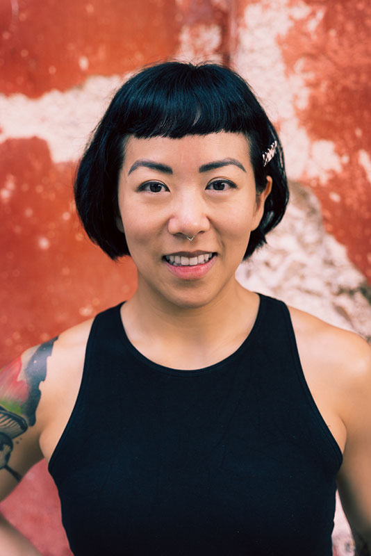 Melody Li's Headshot Melody Li's Headshot: middle-age East Asian femme-presenting human with medium tone skin, bob haircut, wearing a black tank top, tattoo on right shoulder, smiling at the viewer.